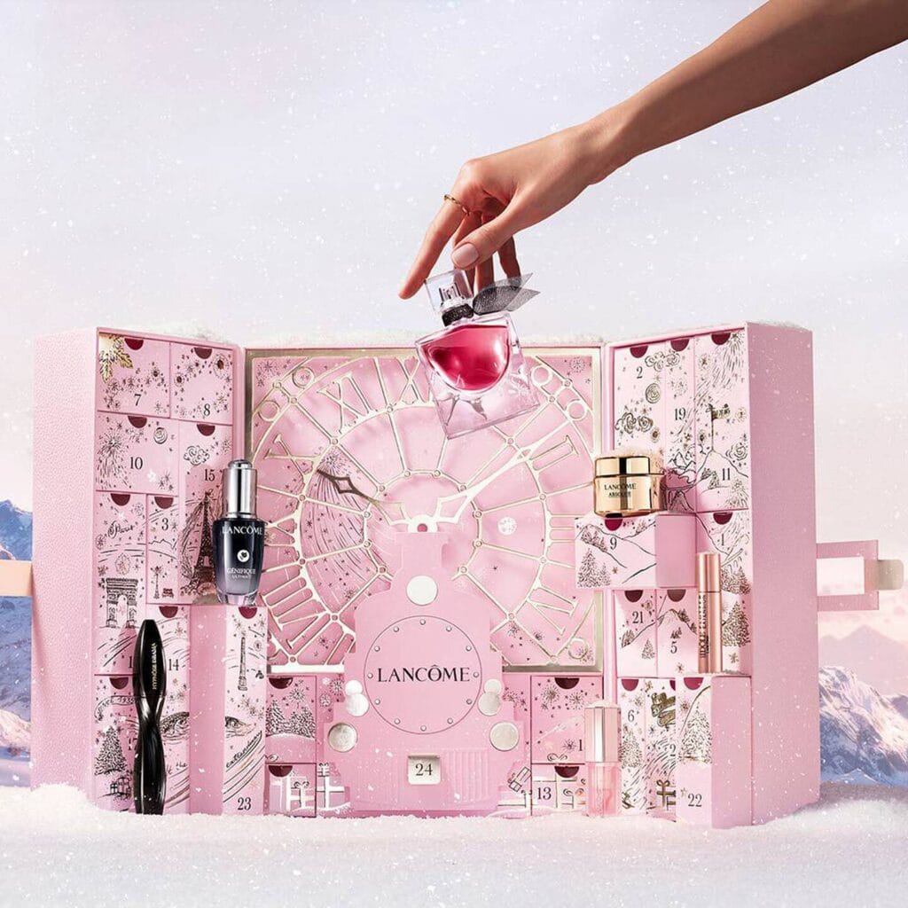 Una mano de mujer coge un perfume de la caja del Calendario de adviento Lancome 2025