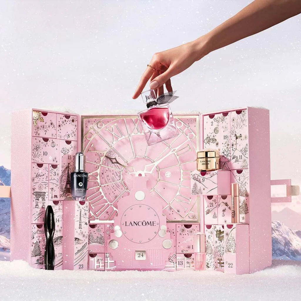 Una mano de mujer coge un perfume de la caja del Calendario de adviento Lancome 2025