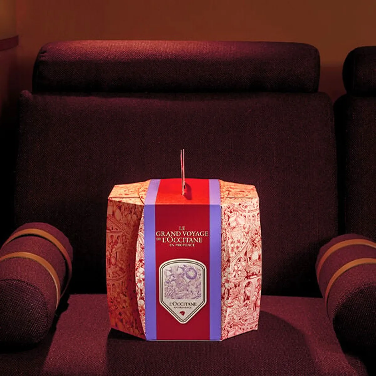 La caja del Calendario Premium L'Occitane 2024 "El Estuche de Viaje de los 24 Tesoros" sobre un sillón