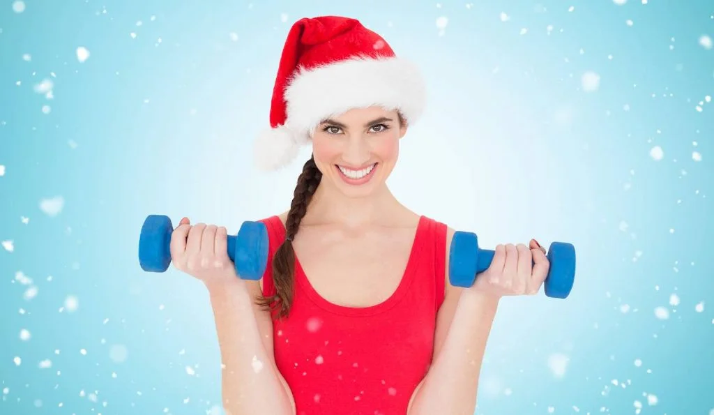 Una chica sonriente con un gorro de Papá Noel levanta unas pesas